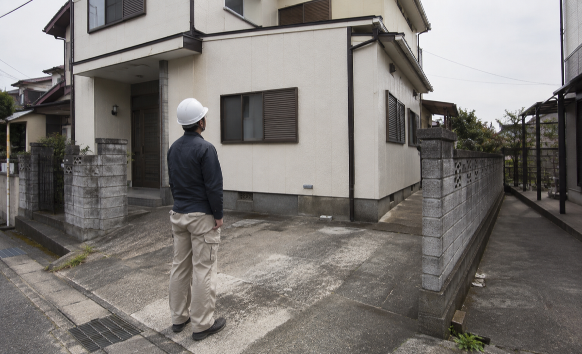 解体業者の担当者が戸建ての外壁、敷地境界、搬入経路を確認している様子